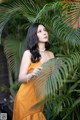 A woman in an orange dress standing next to a palm tree.