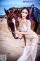 A woman in a white dress standing next to a brown horse.