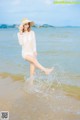 A woman in a white dress and hat standing in the water.