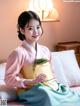 A woman in a pink and blue hanbok sitting on a bed.