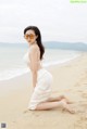 A woman in a white bikini sitting on the beach.