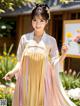 A woman in a pink and yellow hanbok standing in a garden.