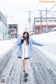 A woman walking down a snow covered road with her arms outstretched.