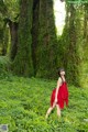 A woman in a red dress standing in the middle of a forest.