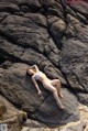 A woman in a white bikini laying on a rock.