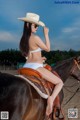 A woman in a white bikini sitting on a brown horse.