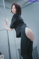 A woman in a black shirt and black pants leaning against a fence.