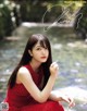 A woman in a red dress sitting on a rock by a river.